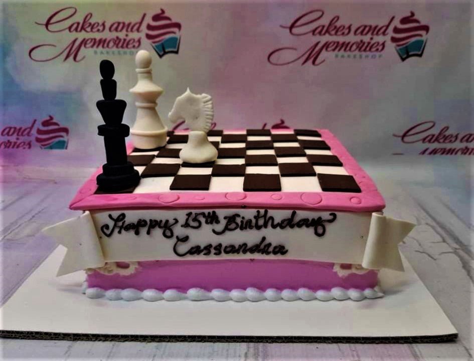 Pink square chess themed birthday cake with black and white fondant chess pieces and a white banner message. Pink square chess themed birthday cake with black and white fondant chess pieces and a white banner message.