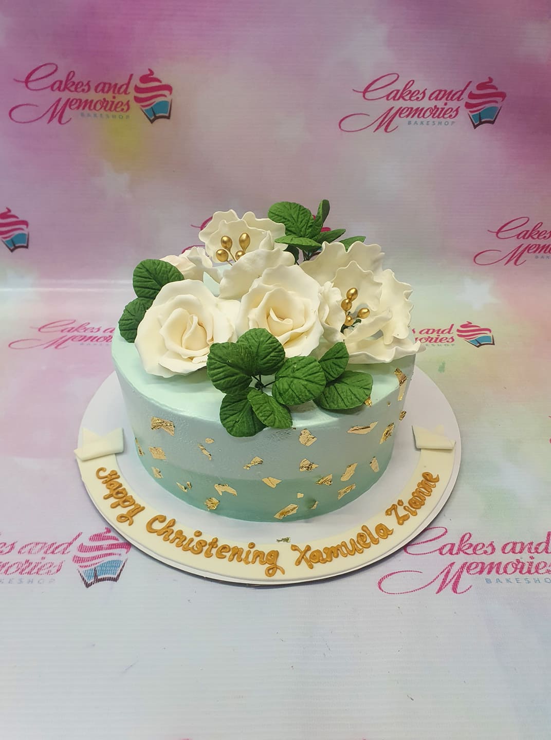 Light blue and teal gradient christening cake with white gumpaste roses, green leaves, and gold leaf accents. Light blue and teal gradient christening cake with white gumpaste roses, green leaves, and gold leaf accents.