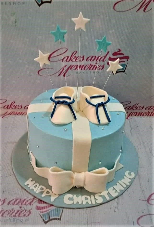 Christening Sky Blue Bow Cake Light blue fondant christening cake with white baby booties, a large white bow, and star toppers on wires.