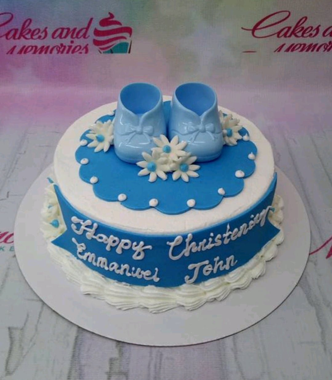 Blue and white christening cake for a boy featuring blue fondant baby shoes and white daisies on a blue scalloped topper. Blue and white christening cake for a boy featuring blue fondant baby shoes and white daisies on a blue scalloped topper.