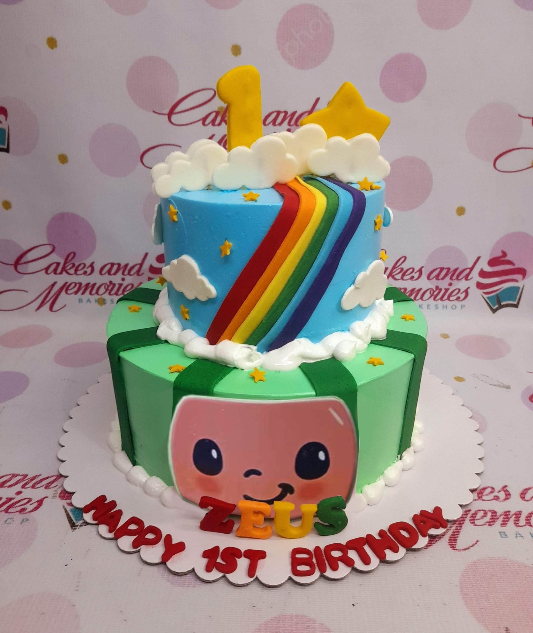 Two-tier Cocomelon themed birthday cake with a blue top tier featuring a rainbow and a green bottom tier with a Cocomelon face. Two-tier Cocomelon themed birthday cake with a blue top tier featuring a rainbow and a green bottom tier with a Cocomelon face.