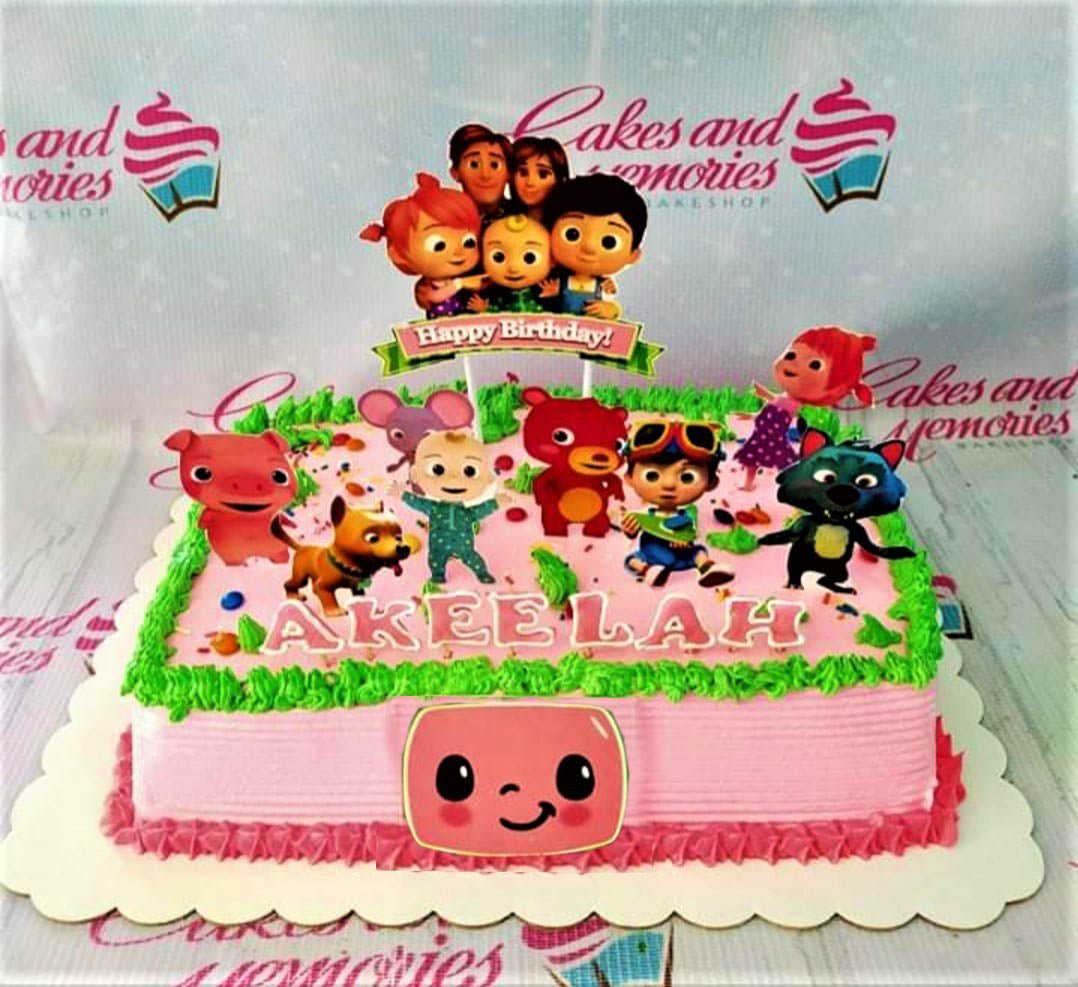 Pink rectangular Cocomelon birthday cake with green icing grass borders and various character printouts. Pink rectangular Cocomelon birthday cake with green icing grass borders and various character printouts.