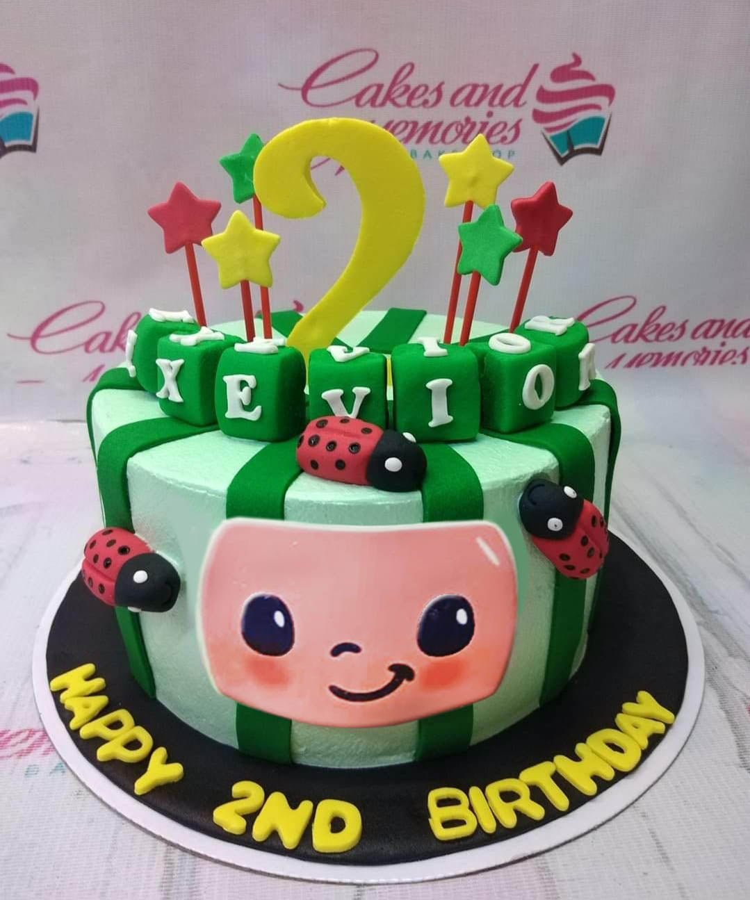 Cocomelon themed birthday cake with green stripes, ladybugs, and a large character face on the side. Cocomelon themed birthday cake with green stripes, ladybugs, and a large character face on the side.