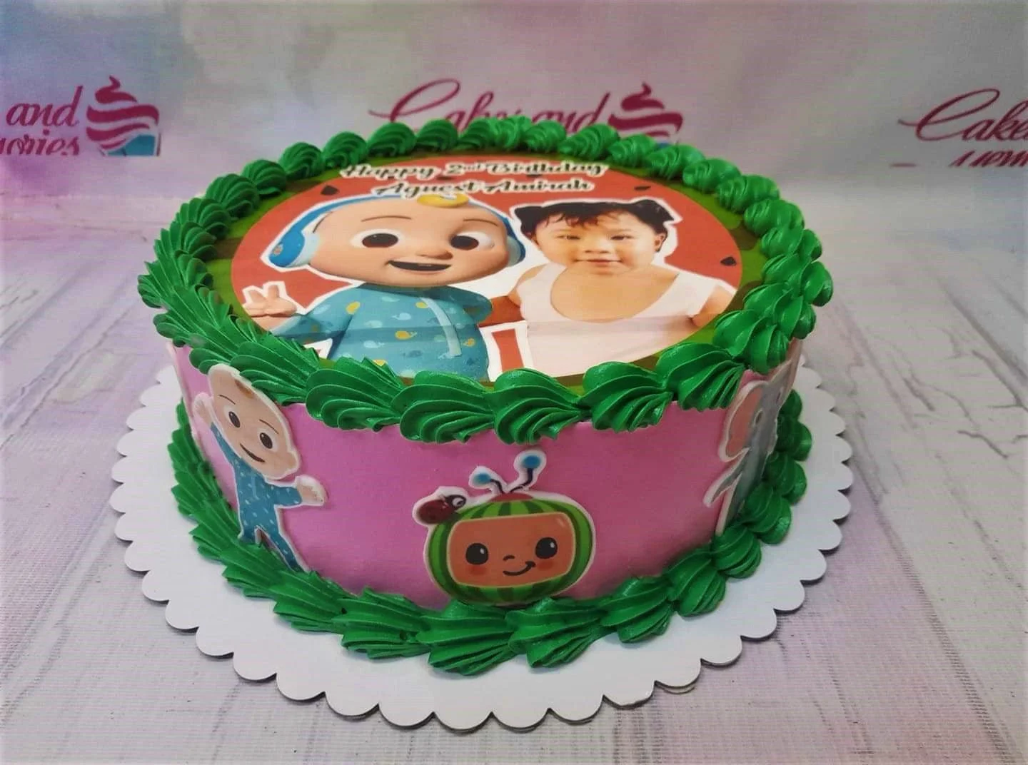 Pink Cocomelon birthday cake with green icing borders and a large edible photo print of a child and JJ. Pink Cocomelon birthday cake with green icing borders and a large edible photo print of a child and JJ.
