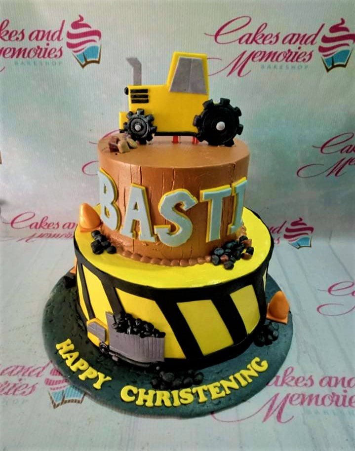 Two-tier construction themed christening cake with a yellow tractor topper, orange cones, and black coal accents on brown and yellow tiers. Two-tier construction themed christening cake with a yellow tractor topper, orange cones, and black coal accents on brown and yellow tiers.