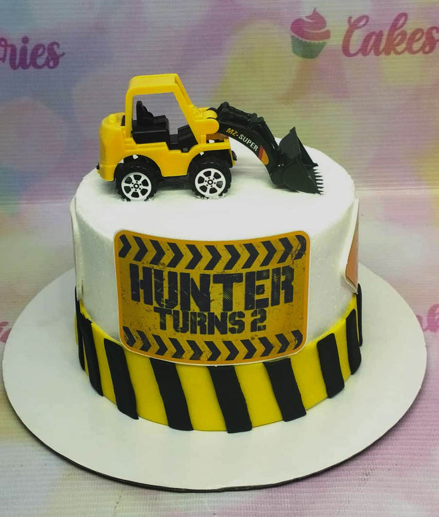Construction themed birthday cake with a yellow toy excavator on top and black and yellow hazard stripes around the base. Construction themed birthday cake with a yellow toy excavator on top and black and yellow hazard stripes around the base.