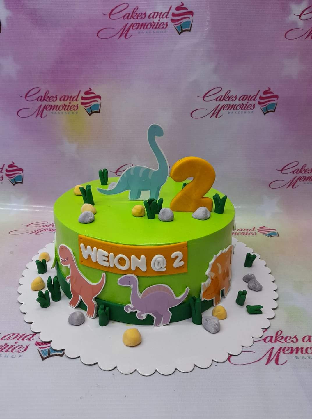 Green dinosaur themed birthday cake with fondant dinosaurs, rocks, and a large yellow number 2 topper. Green dinosaur themed birthday cake with fondant dinosaurs, rocks, and a large yellow number 2 topper.