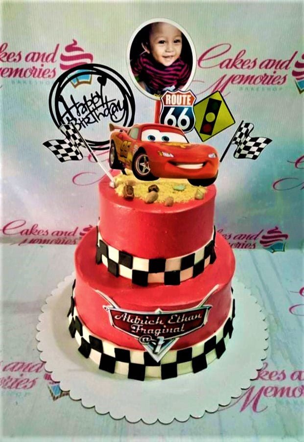 Red 2-tier Disney Cars themed birthday cake with Lightning McQueen topper and checkered racing flag patterns. Red 2-tier Disney Cars themed birthday cake with Lightning McQueen topper and checkered racing flag patterns.
