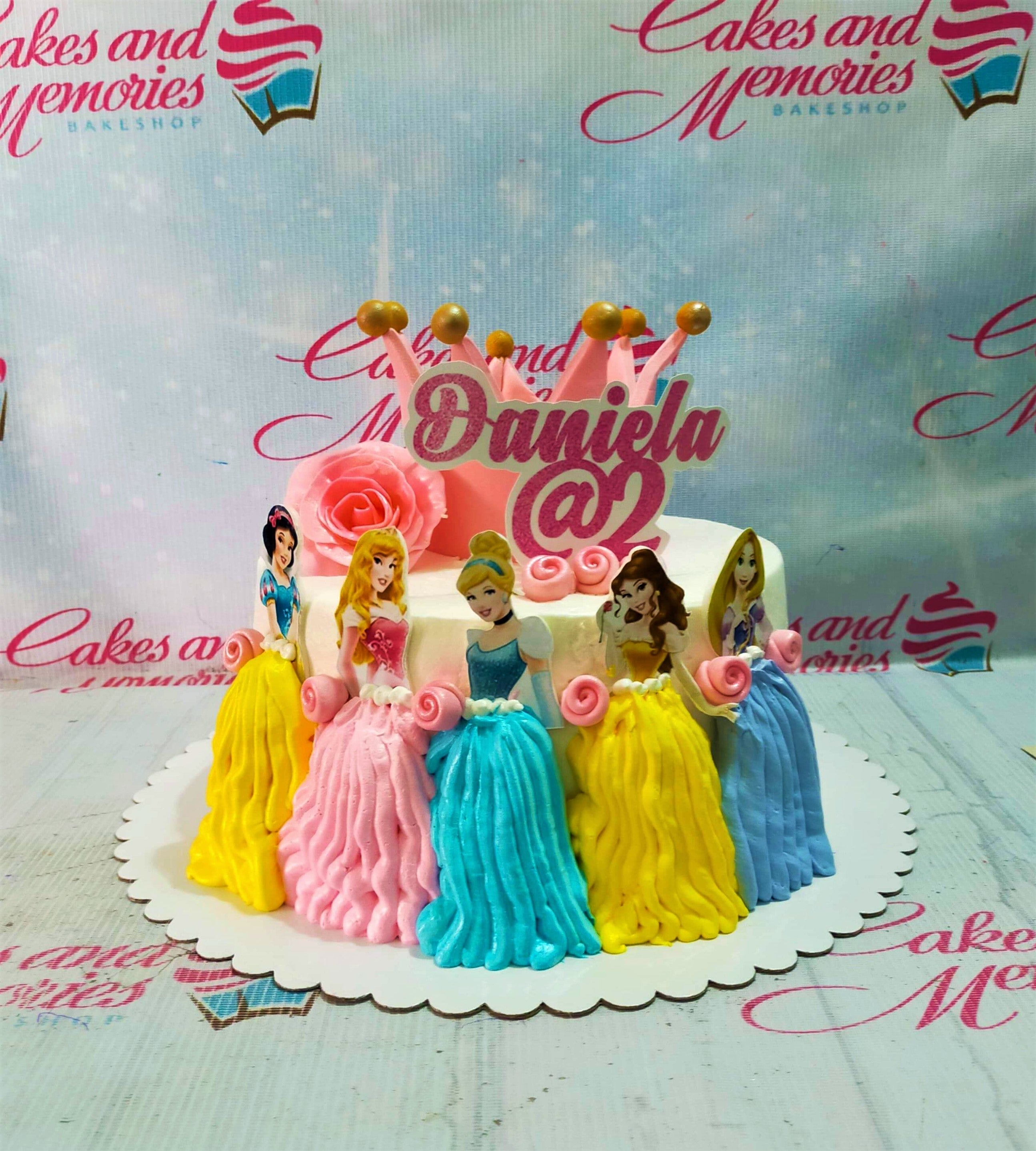 White 1-tier Disney Princess cake with Snow White, Aurora, Cinderella, Belle, and Rapunzel printouts and a pink crown topper. White 1-tier Disney Princess cake with Snow White, Aurora, Cinderella, Belle, and Rapunzel printouts and a pink crown topper.