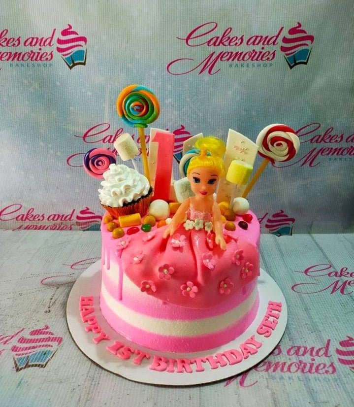Pink and white striped doll cake with a blonde doll topper, lollipops, marshmallows, and a cupcake decoration. Pink and white striped doll cake with a blonde doll topper, lollipops, marshmallows, and a cupcake decoration.