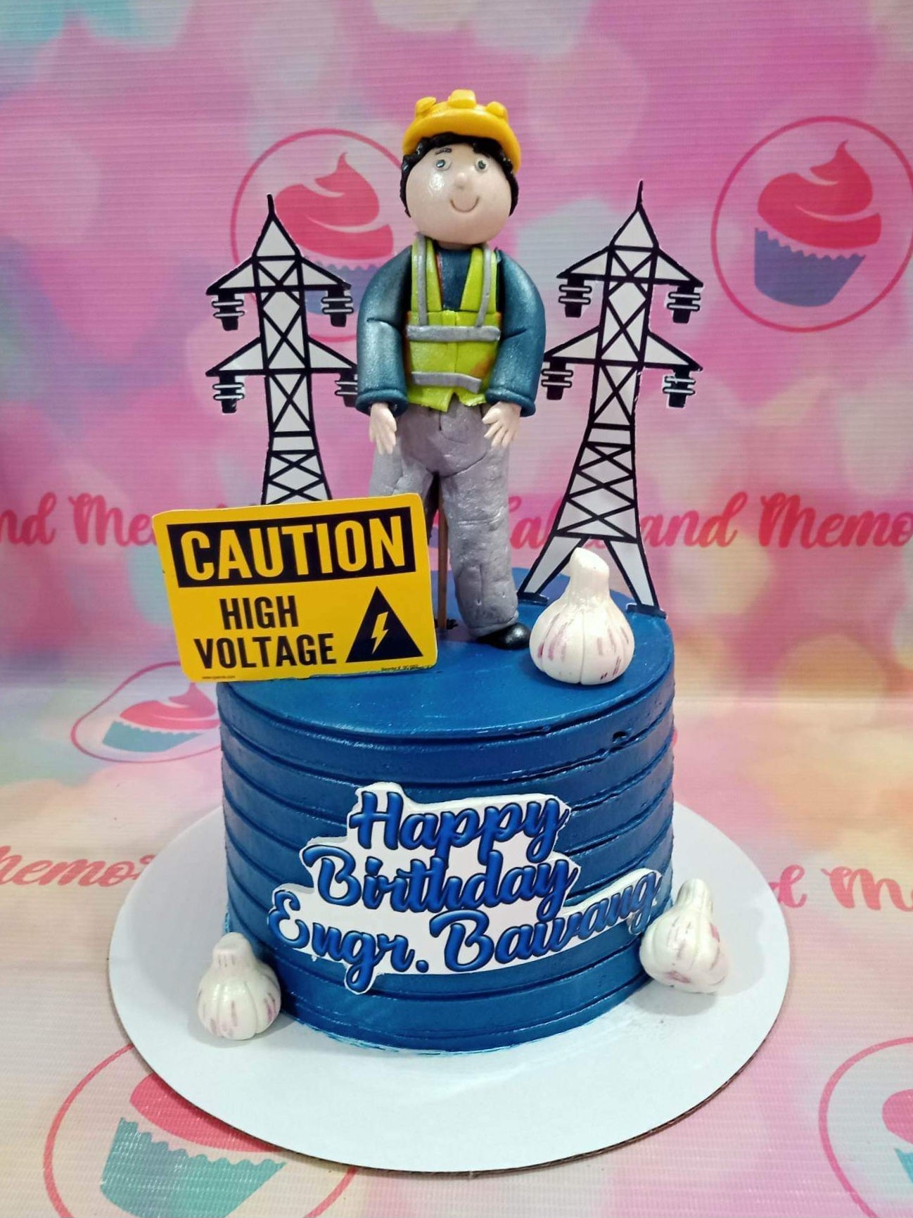 Blue electrical engineer birthday cake with a fondant lineman figure, power line towers, and garlic bulb decorations. Blue electrical engineer birthday cake with a fondant lineman figure, power line towers, and garlic bulb decorations.