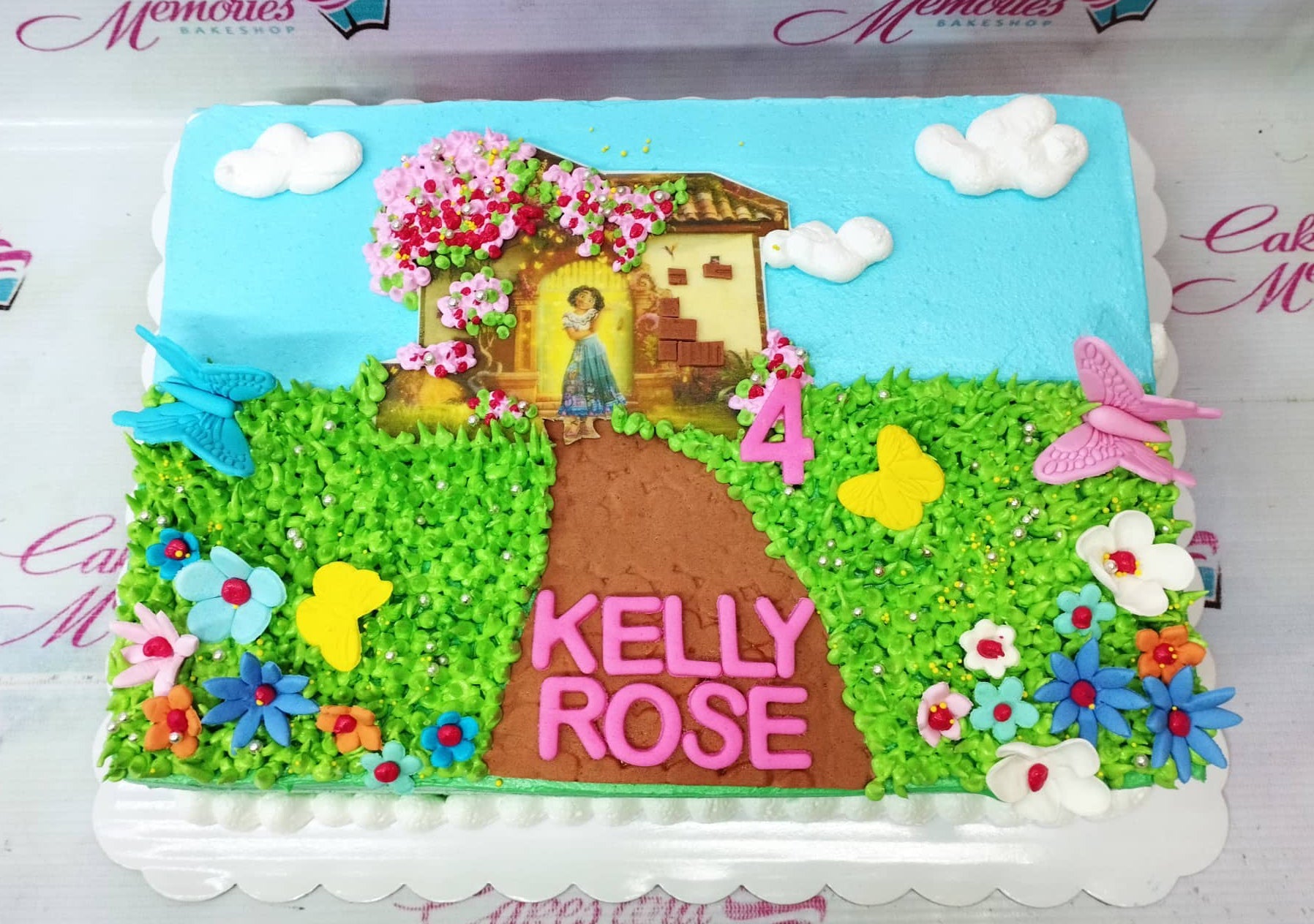Encanto themed rectangle cake with a printed house topper, green grass icing, and pink fondant name letters. Encanto themed rectangle cake with a printed house topper, green grass icing, and pink fondant name letters.