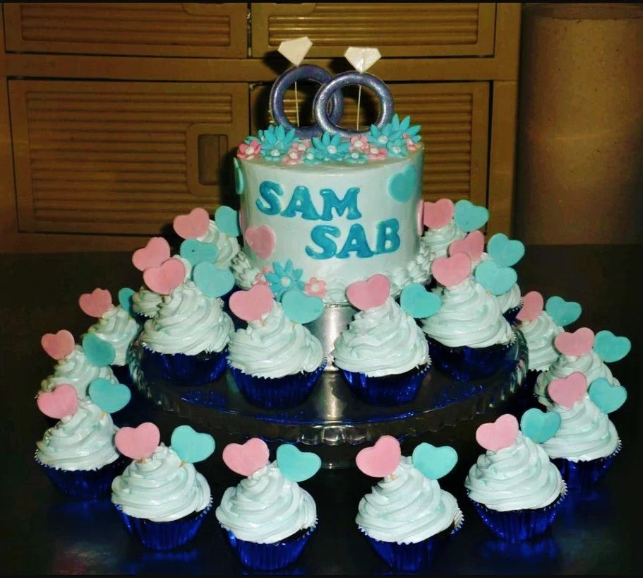 Engagement Sky Blue Heart Cake Light blue single tier cake with blue and pink heart toppers and matching cupcakes on a glass stand.