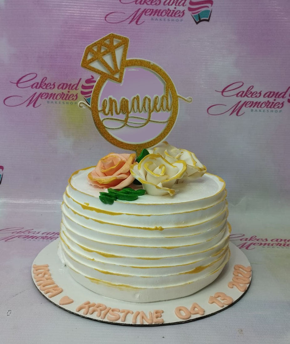 White 1-tier engagement cake with horizontal icing ridges, gold accents, peach and white roses, and a gold 'engaged' ring topper. White 1-tier engagement cake with horizontal icing ridges, gold accents, peach and white roses, and a gold 'engaged' ring topper.