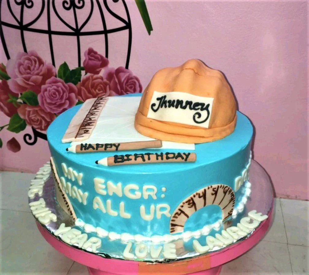 Light blue engineering themed birthday cake with a fondant hard hat, ruler, pencils, and protractor decorations. Light blue engineering themed birthday cake with a fondant hard hat, ruler, pencils, and protractor decorations.