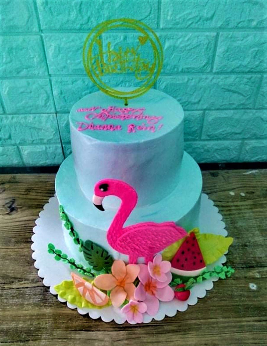 Two-tier light blue tropical flamingo cake with pink flamingo topper, watermelon, and floral decorations. Two-tier light blue tropical flamingo cake with pink flamingo topper, watermelon, and floral decorations.
