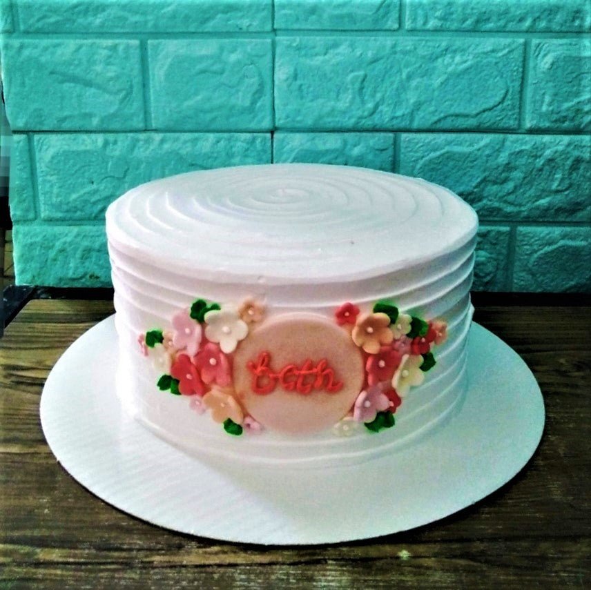 White textured soft icing cake with a central pink fondant plaque and a cluster of colorful edible flowers. White textured soft icing cake with a central pink fondant plaque and a cluster of colorful edible flowers.