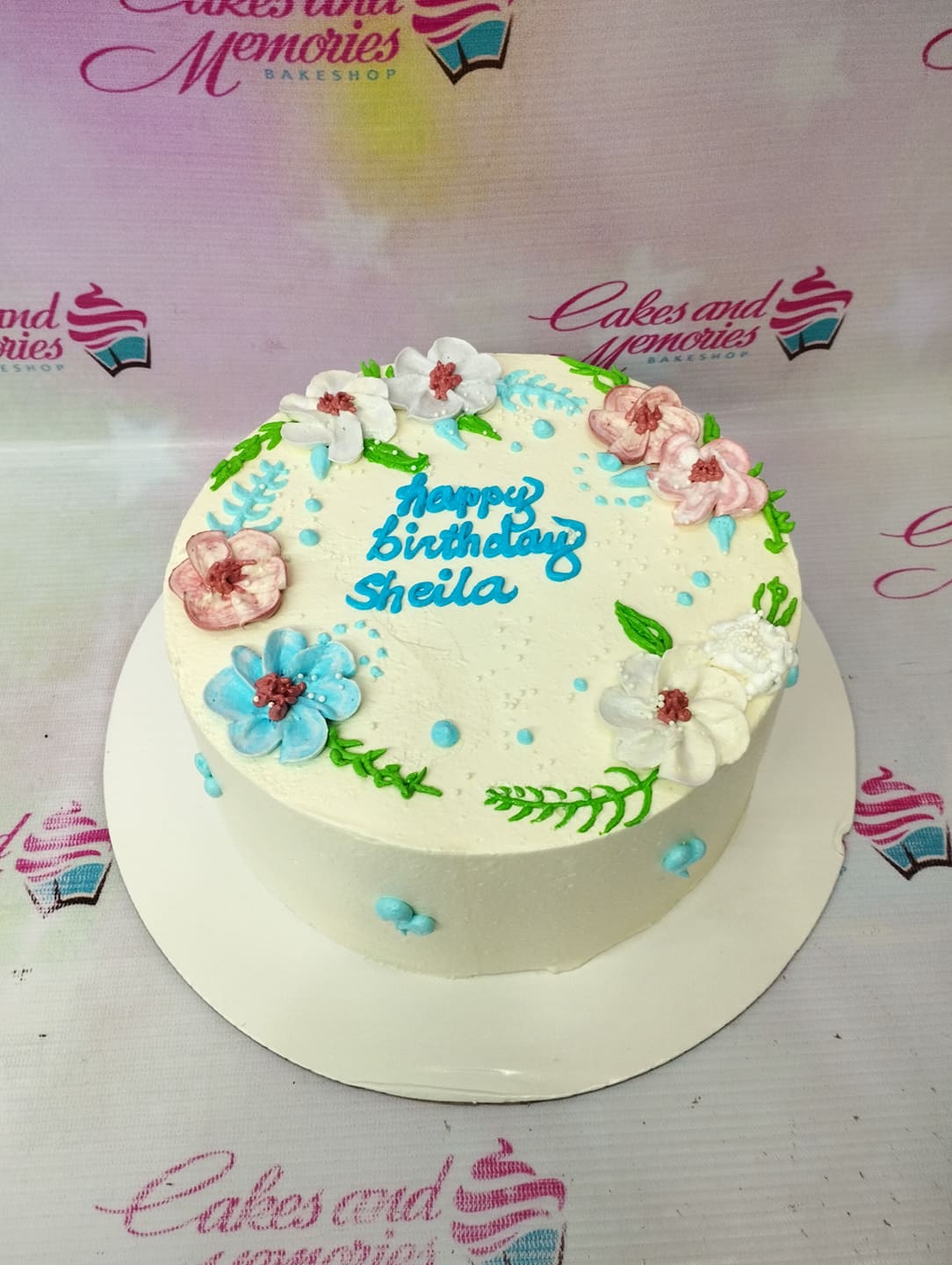 White soft-icing birthday cake decorated with colorful piped icing flowers and a blue birthday message. White soft-icing birthday cake decorated with colorful piped icing flowers and a blue birthday message.