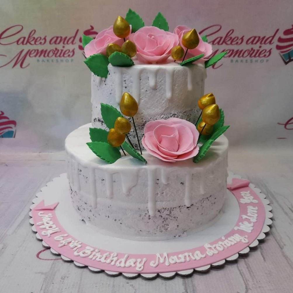 Two-tier semi-naked chocolate cake with white icing drips, pink fondant roses, and gold decorative buds on a pink base board. Two-tier semi-naked chocolate cake with white icing drips, pink fondant roses, and gold decorative buds on a pink base board.