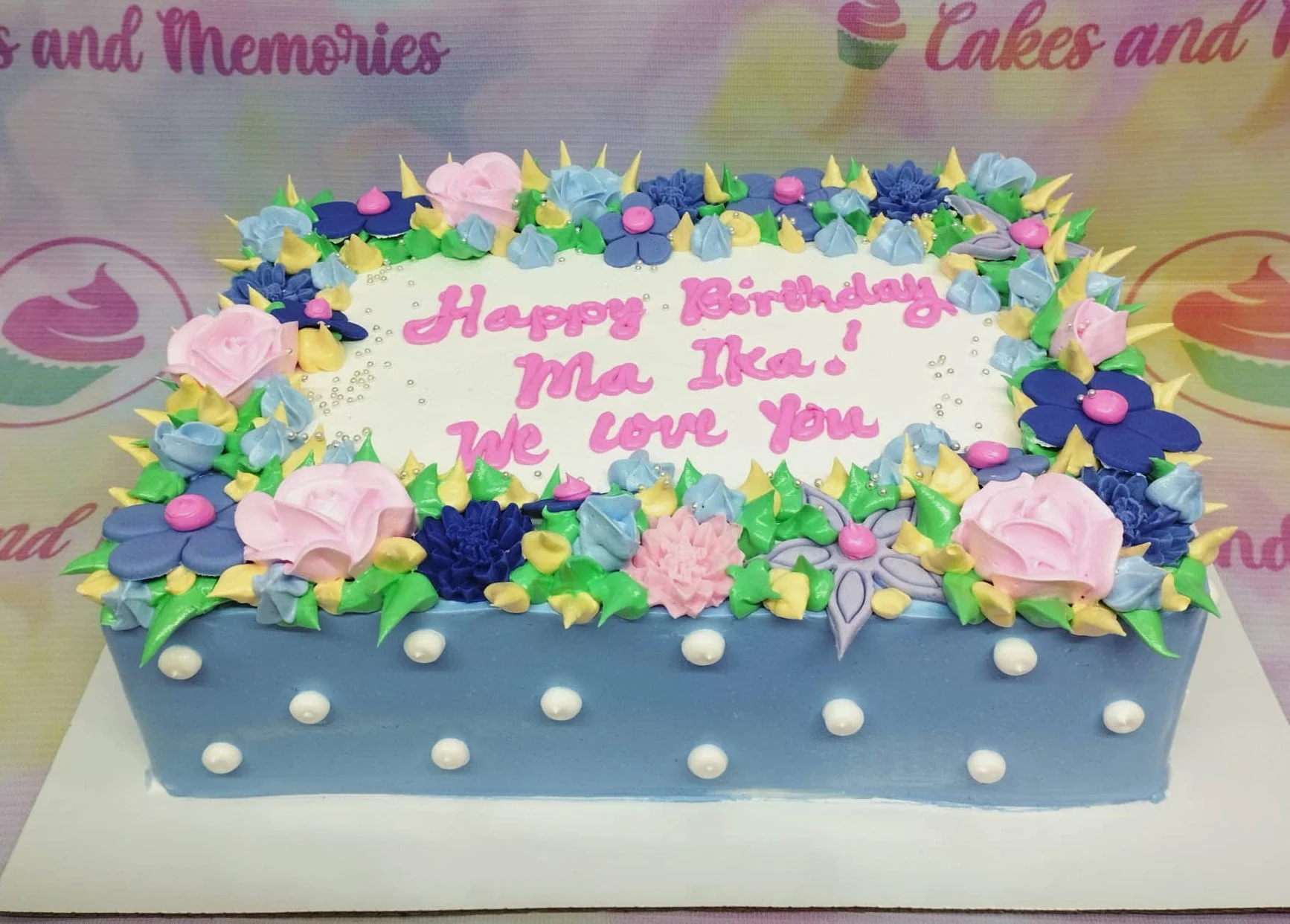 Floral Birthday Rectangle Dedication Cake A light blue Rectangle cake with white top, Floral Birthday theme, featuring a pink icing message, colorful flowers, and silver dragees.