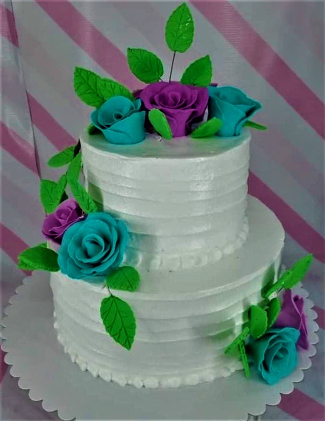 Two-tier white soft-icing cake decorated with teal and purple gumpaste roses and green leaves. Two-tier white soft-icing cake decorated with teal and purple gumpaste roses and green leaves.