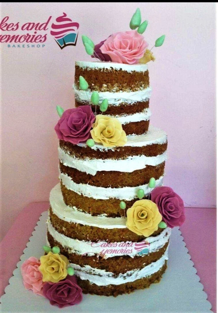 Three-tier naked cake with exposed chocolate layers and white icing, decorated with pink, purple, and yellow gumpaste roses and green buds.