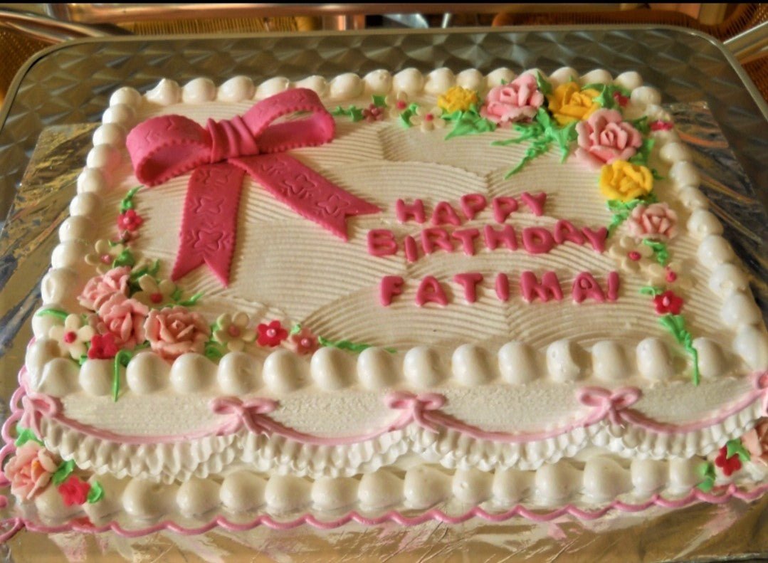 White rectangular cake with pink icing ruffles, a large pink fondant bow, and colorful icing flowers for Fatima's birthday. White rectangular cake with pink icing ruffles, a large pink fondant bow, and colorful icing flowers for Fatima's birthday.