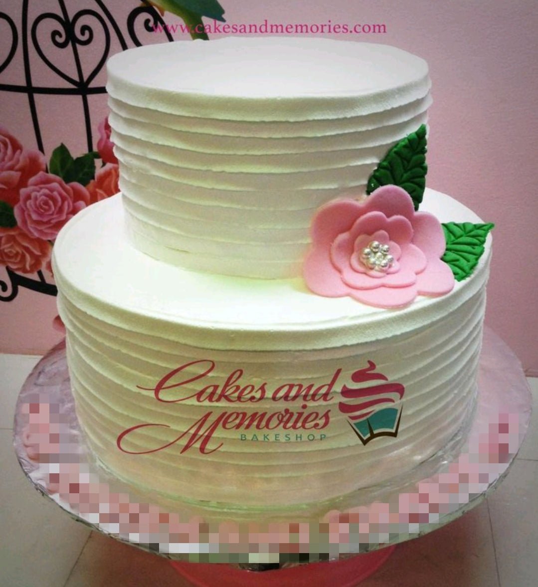 Elegant white 2-tier cake with horizontal textured icing and a large pink fondant flower with pearl center and green leaves. Elegant white 2-tier cake with horizontal textured icing and a large pink fondant flower with pearl center and green leaves.