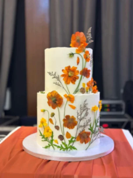 Floral White 2-Tier Cake Elegant two-tier white cake decorated with vibrant orange and yellow pressed flowers and green stems