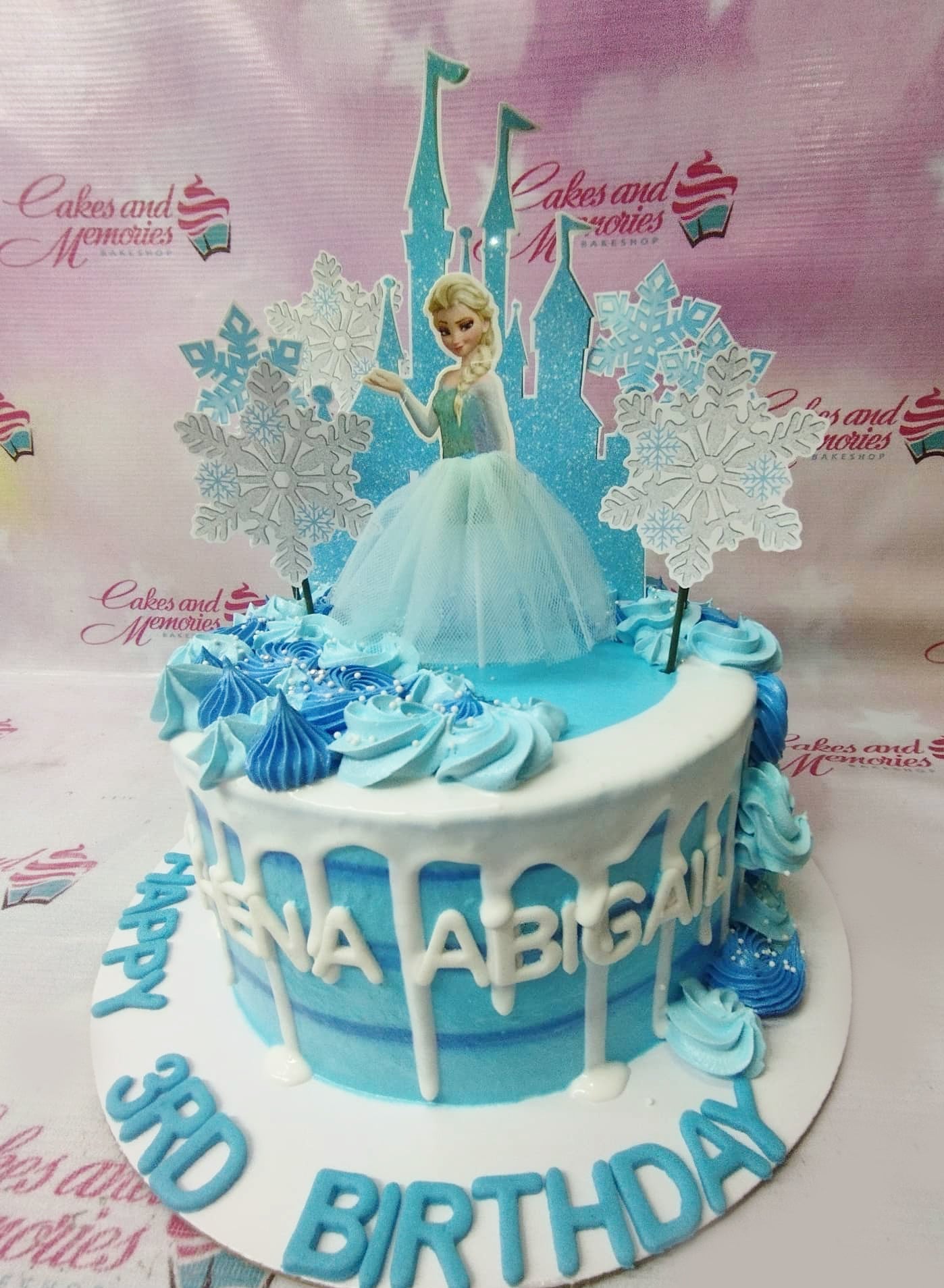 Blue and white Frozen themed birthday cake with Elsa printout topper, castle backdrop, and white icing drips. Blue and white Frozen themed birthday cake with Elsa printout topper, castle backdrop, and white icing drips.