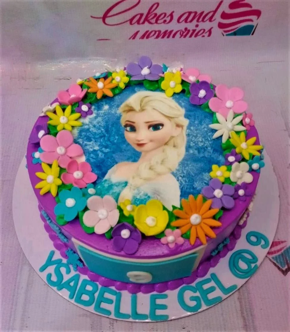 Purple Frozen themed cake featuring a large Elsa printout surrounded by colorful fondant flowers and a blue name plaque.