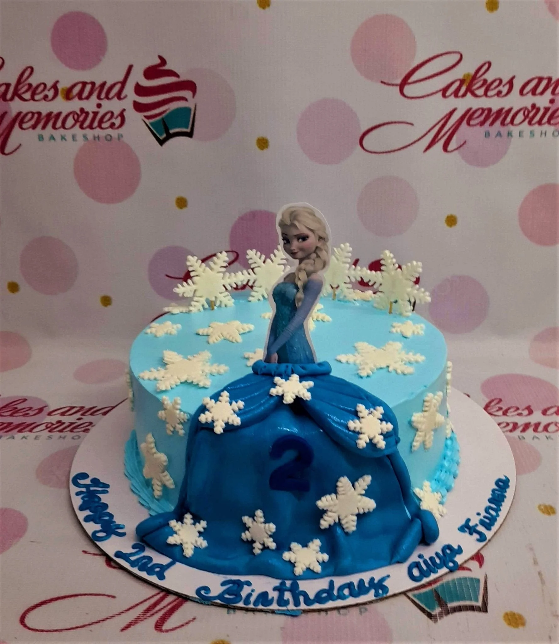 Light blue Frozen themed cake with Elsa printout topper, white fondant snowflakes, and a blue fondant dress drape with a number 2.