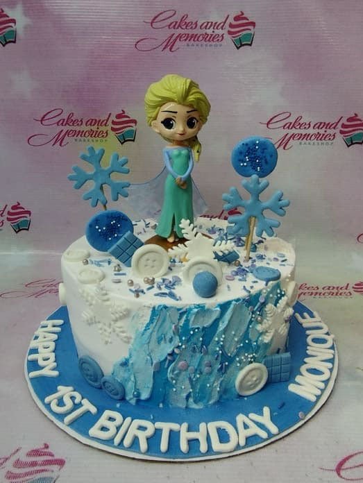 Frozen Elsa themed birthday cake with blue and white icing, snowflakes, and a 3D Elsa figurine on a blue base board. Frozen Elsa themed birthday cake with blue and white icing, snowflakes, and a 3D Elsa figurine on a blue base board.