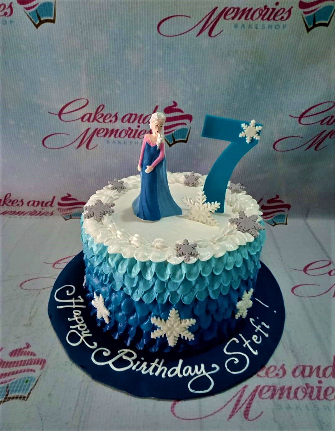 Blue ombre ruffled icing cake with Elsa figurine, large blue number 7, and white snowflake decorations. Blue ombre ruffled icing cake with Elsa figurine, large blue number 7, and white snowflake decorations.