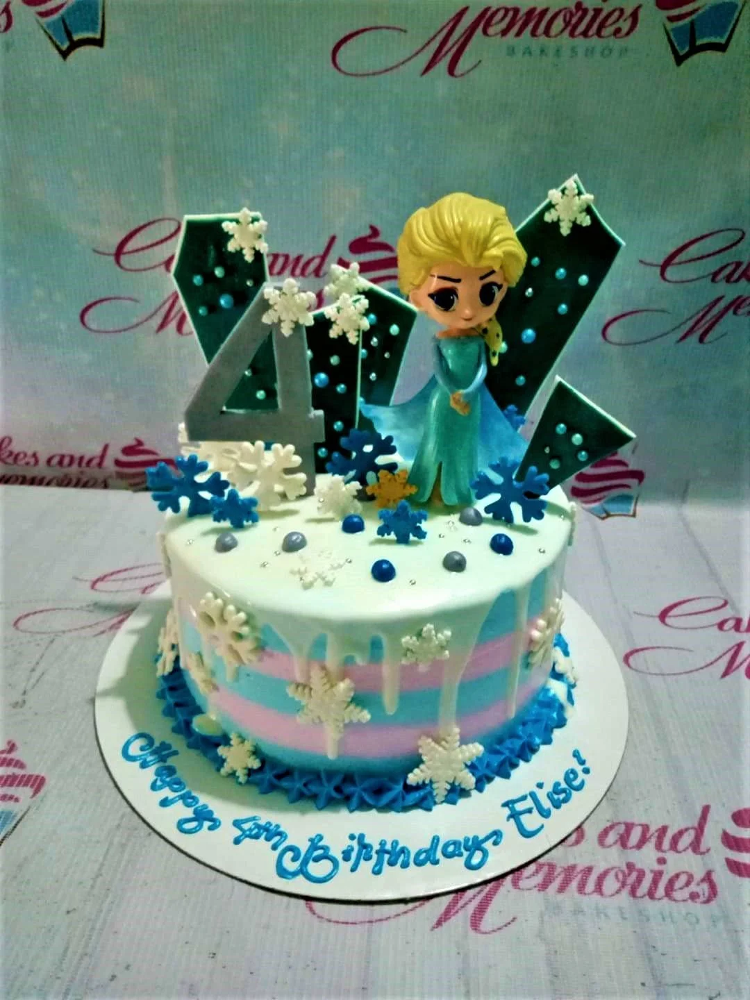 Frozen-Inspired Elsa Birthday Cake A blue and pink 1-Tier Frozen Elsa cake, featuring an Elsa figurine, number 4, snowflake decorations.