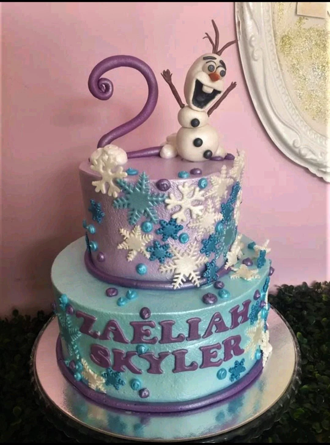 Two-tier Frozen themed cake in light blue and purple with Olaf figurine, snowflakes, and a large purple number two topper.