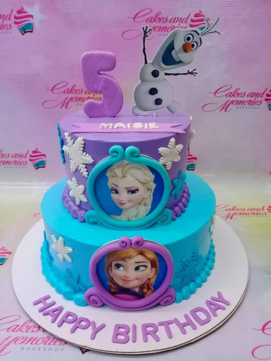 Two-tier Frozen themed cake in purple and light blue with Elsa, Anna, and Olaf toppers and snowflake decorations. Two-tier Frozen themed cake in purple and light blue with Elsa, Anna, and Olaf toppers and snowflake decorations.
