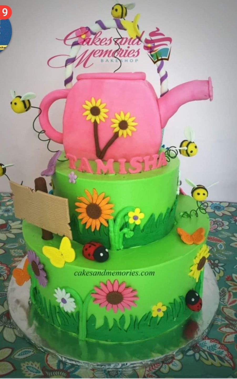 Two-tier green garden themed cake with a pink watering can topper, sunflowers, bees, and ladybugs. Two-tier green garden themed cake with a pink watering can topper, sunflowers, bees, and ladybugs.