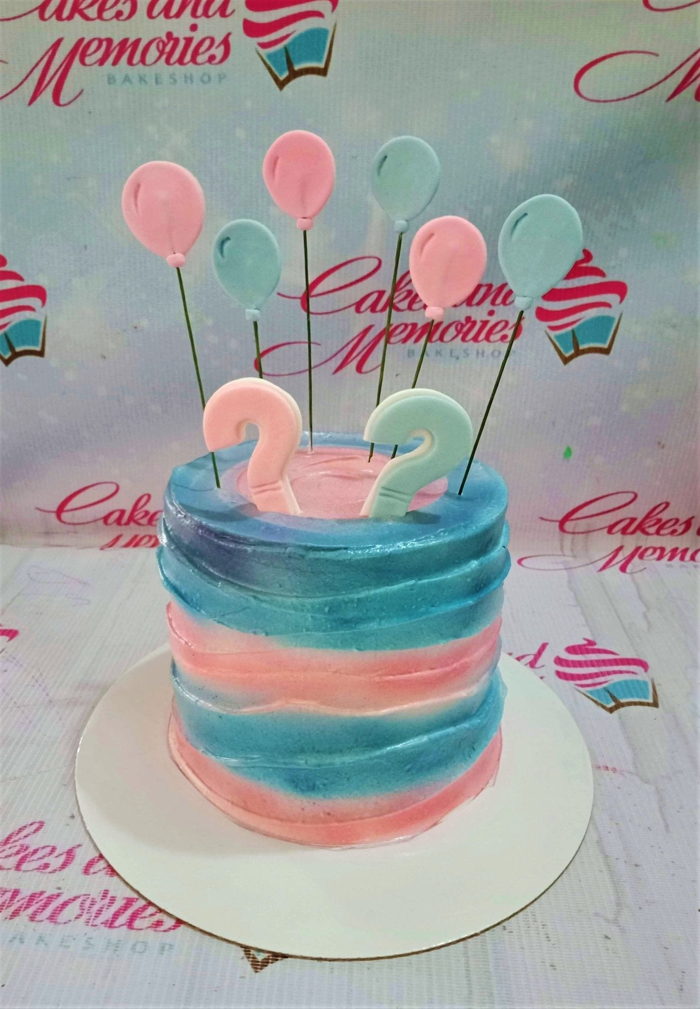 Gender reveal cake with pink and blue horizontal icing stripes, topped with fondant balloons and question marks. Gender reveal cake with pink and blue horizontal icing stripes, topped with fondant balloons and question marks.