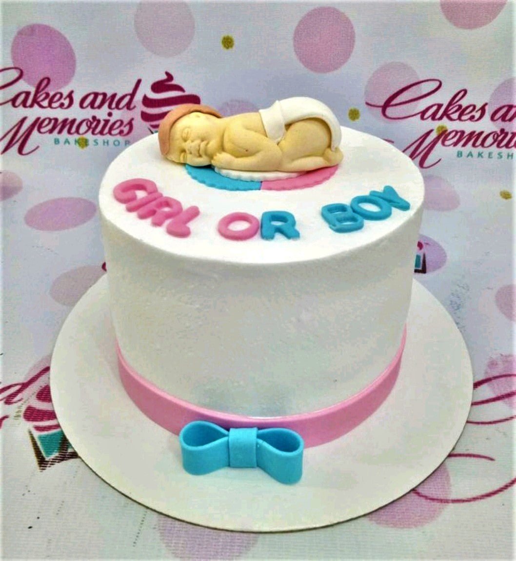 White gender reveal cake with a sleeping fondant baby topper on a pink and blue base and a pink ribbon at the bottom. White gender reveal cake with a sleeping fondant baby topper on a pink and blue base and a pink ribbon at the bottom.