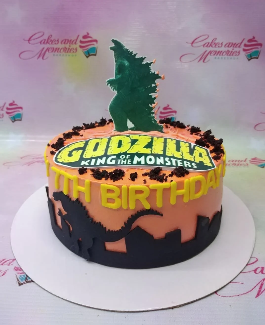Orange Godzilla King of the Monsters birthday cake with black city skyline silhouette and green Godzilla topper. Orange Godzilla King of the Monsters birthday cake with black city skyline silhouette and green Godzilla topper.
