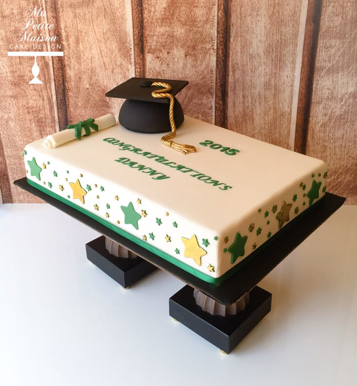 White rectangular graduation cake with a black fondant graduation cap, gold tassel, white scroll, and green and gold stars. White rectangular graduation cake with a black fondant graduation cap, gold tassel, white scroll, and green and gold stars.