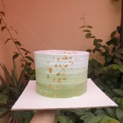 A single tier cake with a green to white gradient horizontal ribbed icing design and gold leaf accents. A single tier cake with a green to white gradient horizontal ribbed icing design and gold leaf accents.