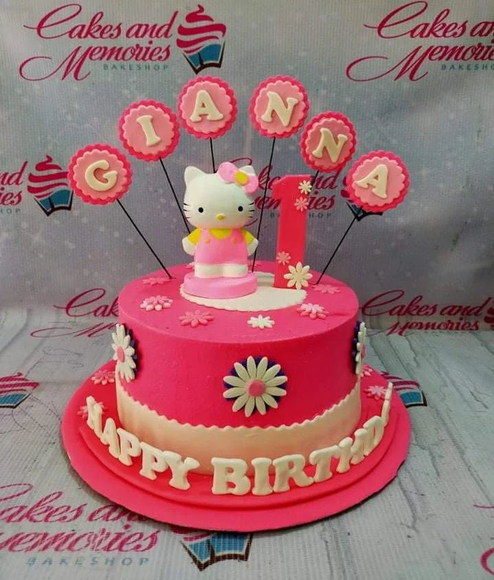 Pink Hello Kitty themed birthday cake with pink and white fondant flowers and personalized name toppers.