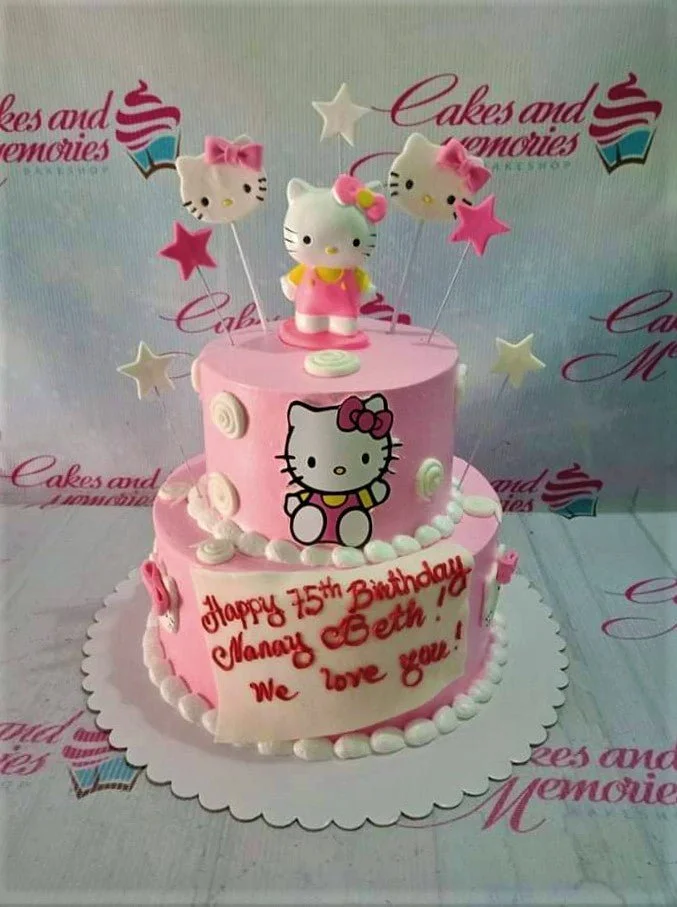 Pink two-tier Hello Kitty birthday cake with fondant figures, stars, and a personalized message on a white plaque.