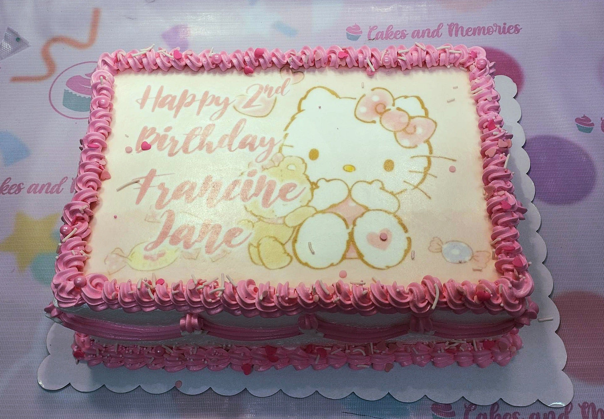Rectangle Hello Kitty birthday cake with pink icing rosettes, heart sprinkles, and a printed edible image of Hello Kitty and a bear. Rectangle Hello Kitty birthday cake with pink icing rosettes, heart sprinkles, and a printed edible image of Hello Kitty and a bear.