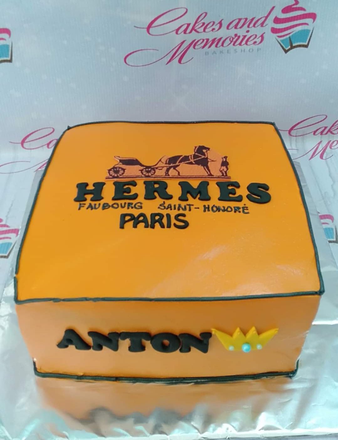 Orange square Hermes themed cake with black logo and name Anton on the side. Orange square Hermes themed cake with black logo and name Anton on the side.