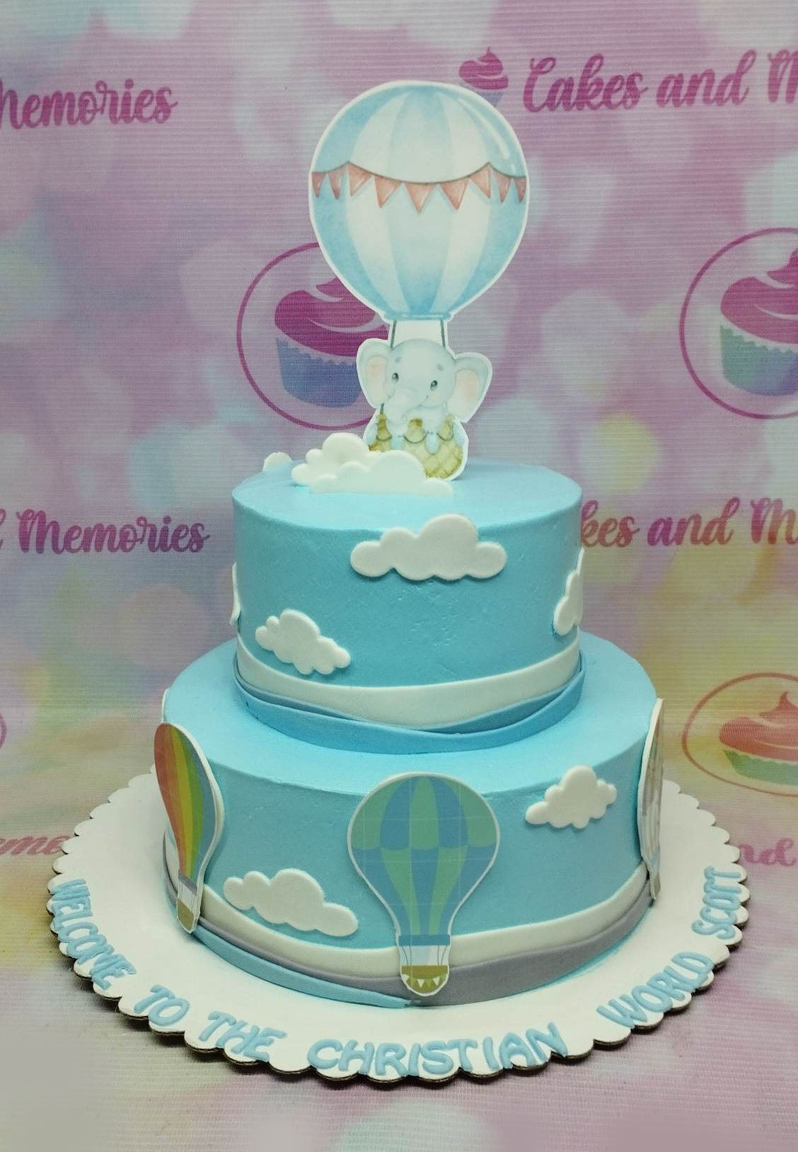 Light blue 2-tier hot air balloon cake with an elephant in a basket topper and white fondant clouds. Light blue 2-tier hot air balloon cake with an elephant in a basket topper and white fondant clouds.