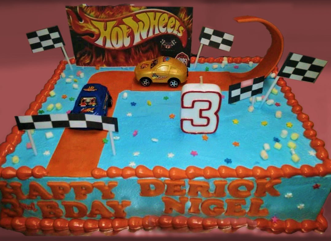 Hot Wheels themed rectangle birthday cake with blue icing, orange racing track, toy cars, and checkered flags for a 3rd birthday. Hot Wheels themed rectangle birthday cake with blue icing, orange racing track, toy cars, and checkered flags for a 3rd birthday.