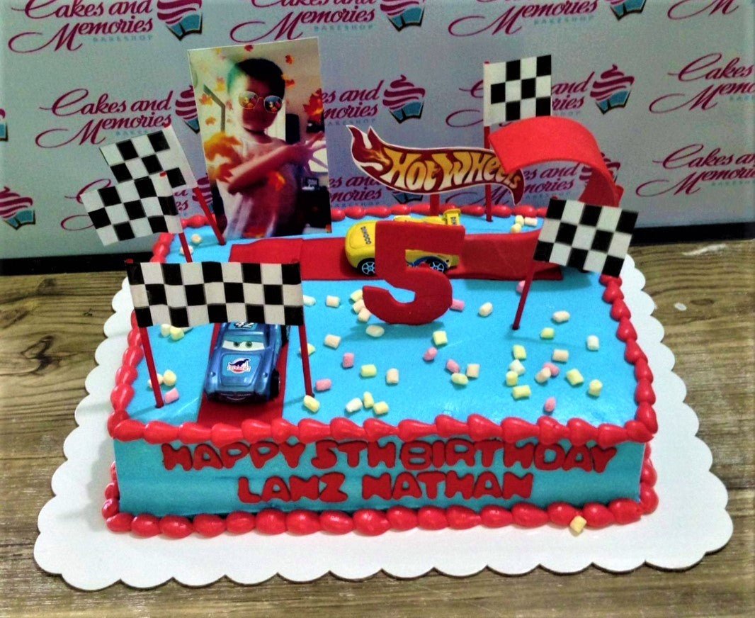 Blue rectangle Hot Wheels and Cars themed birthday cake with a photo printout, toy cars, and checkered flags. Blue rectangle Hot Wheels and Cars themed birthday cake with a photo printout, toy cars, and checkered flags.